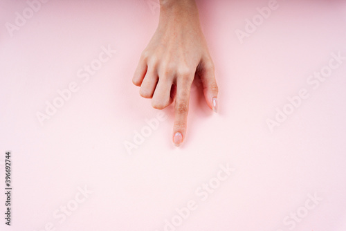 Hand pointing at empty area on pink background.