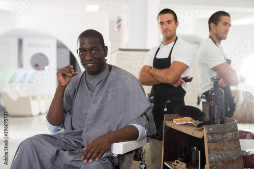 African-American man approving result of hairdresser work, looking satisfied with his new hairdo