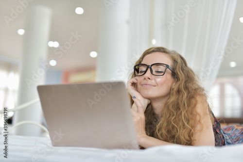 A beautiful woman is enjoying a computer in bed in the bedroom. View various information on social and online. Stay home during the COVID-19 epidemic