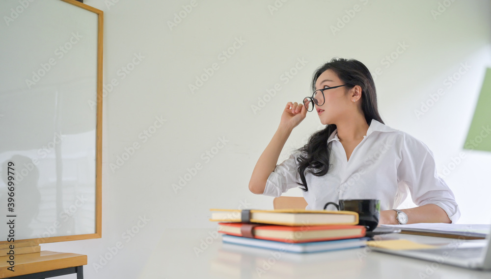 Young working woman holding glasses and looking at the white board in the office. Young working woman holding glasses and looking at the white board in the office.