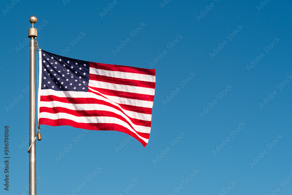 Fototapeta premium Picturesque perfect American flag blowing in the breeze over sky blue background with copy space 