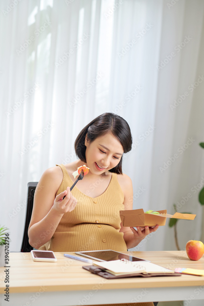 Pregnant woman eating salad while working on digital tablet Pregnant woman eating salad while working on digital tablet