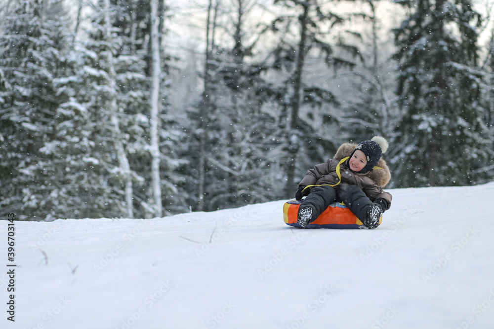 A child riding a tubing from a snow slide in a winter forest. Image with selective focus.