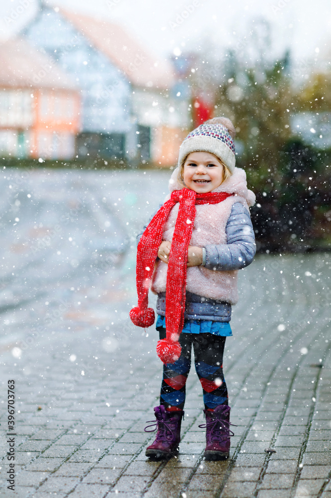 Foto de Cute little funny toddler girl in colorful winter fashion clothes  having fun and playing with snow, outdoors during snowfall. Active outdoors  leisure with children. Happy healthy child do Stock