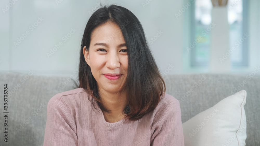 Teenager Asian woman feeling happy smiling and looking to camera while relax in living room at home. Lifestyle beautiful Asian young female using relax time at home concept.