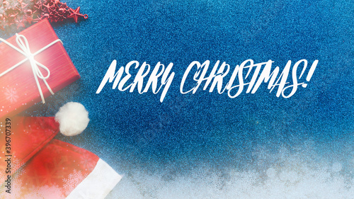 New Year concept. Santa Claus hat, gift, toy tree on a blue glitter background with the inscription.