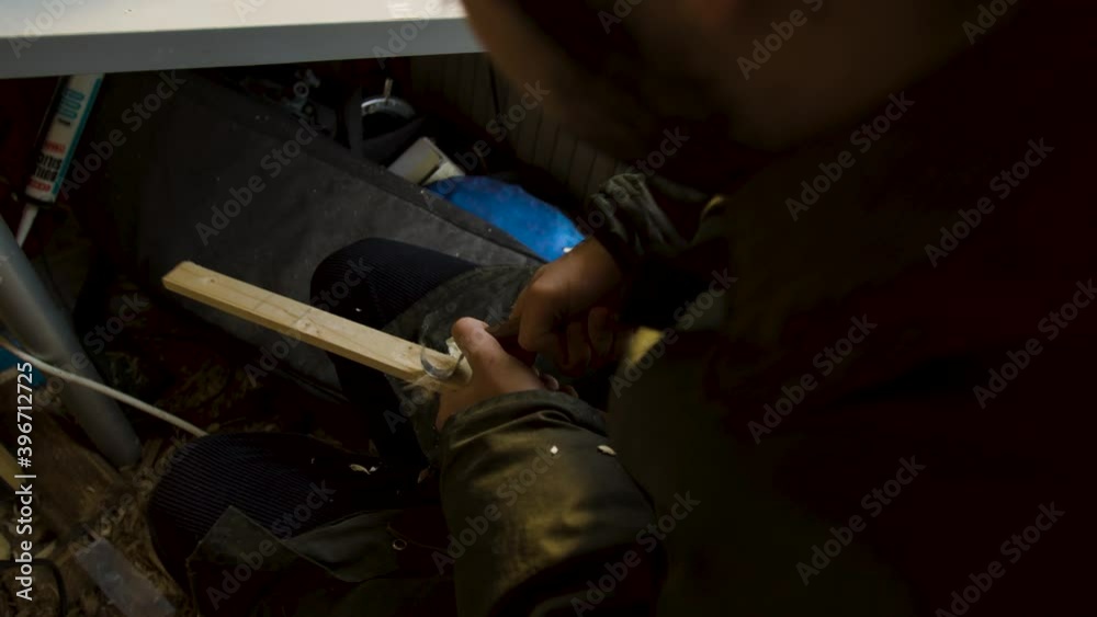 Man woodworking, carving into a long piece of wood with a small knife