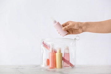 Female hand and bag with travel bottles of body care cosmetics on light background