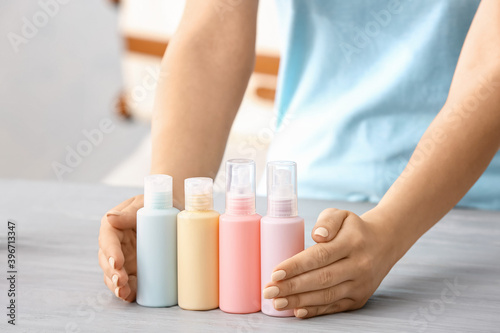 Female hands and set of travel bottles with body care cosmetics on table