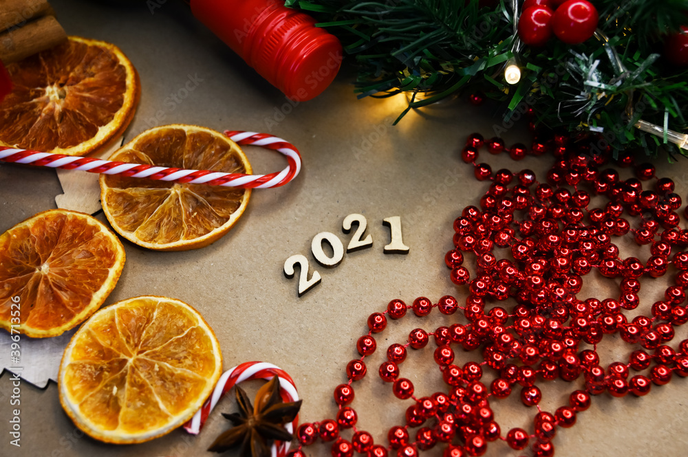 2021 in wooden letters on craft background with candy canes, cinamon, ornaments, fir tree, bottle and dry oranges. New year concept. Festive concept. Happy new 2021 year. Background for post card.