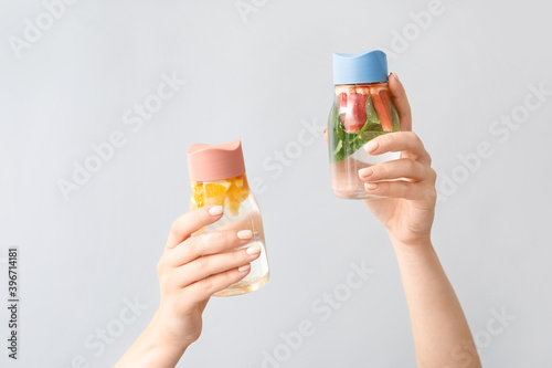 Female hands and bottles of infused water with citruses on light background
