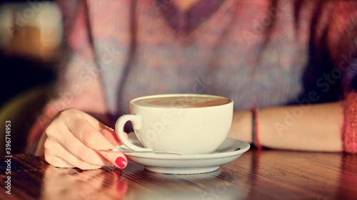 woman hands with latte on a wood table. woman with red nails holds coffee in her hands.