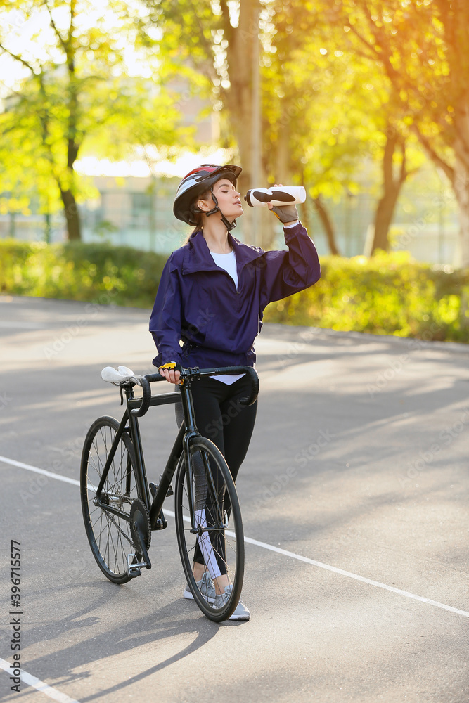 Obraz premium Female cyclist with bicycle drinking water outdoors
