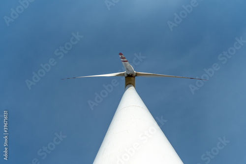 bottom view of a modern windmill against a blue sky. The white blades of the wind turbine. Clean and renewable energy production. pipe and supporting base windmill  close up