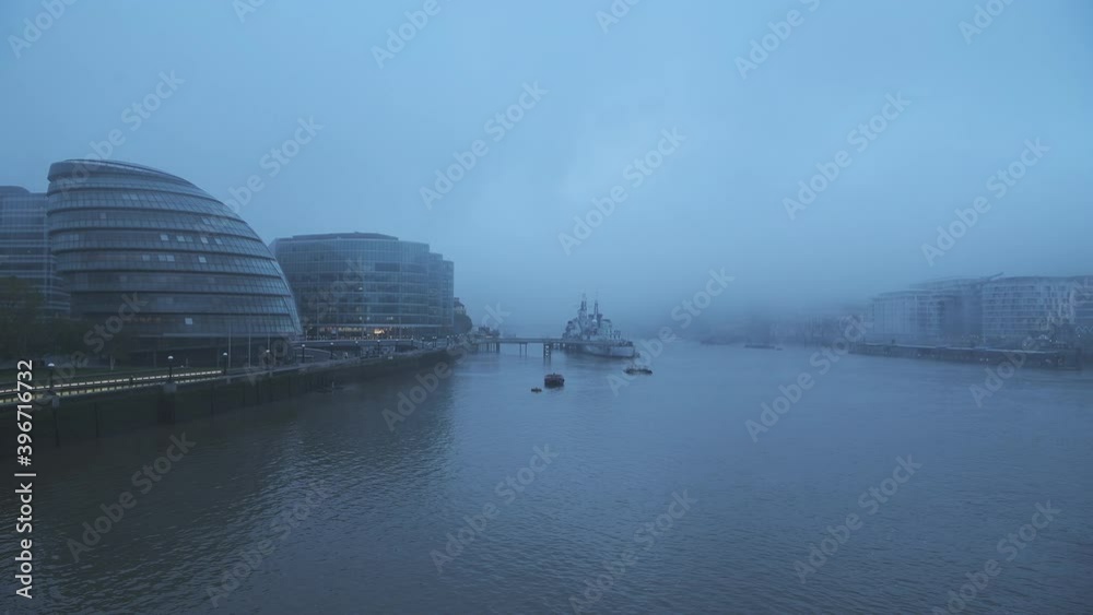 Foggy and misty River Thames in London on Coronavirus Covid-19 lockdown day one, in atmospheric weather with moody blue mist and fog around HMS Belfast and City Hall by Tower Bridge, England, UK Foggy and misty River Thames in London on Coronavirus Covid-19 lockdown day one, in atmospheric weather with moody blue mist and fog around HMS Belfast and City Hall by Tower Bridge, England, UK