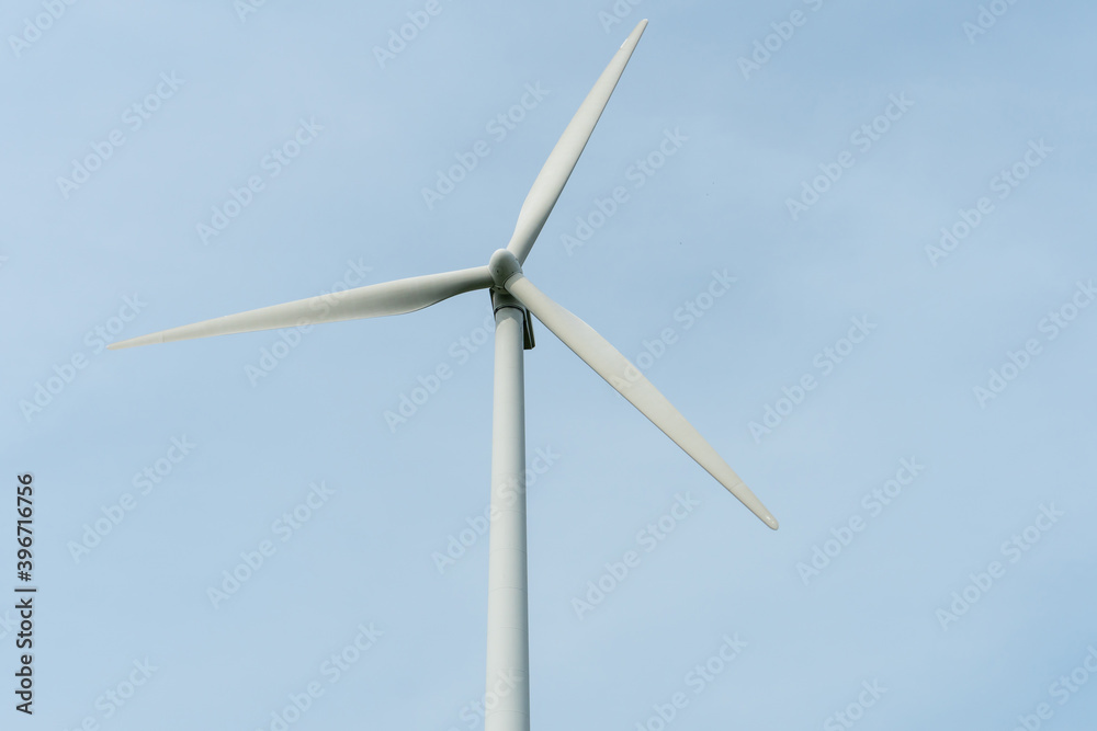 view of a modern windmill against a blue sky. The white blades of the wind turbine close up. Renewable energy source. Production of cheap and safe electricity. view of a modern windmill against a blue sky. The white blades of the wind turbine close up. Renewable energy source. Production of cheap and safe electricity.