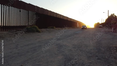 Smooth dolly shot of big car slowly advancing along the notorious U.S. - Mexico border fence, with the sun rising behind it and shining onto the cloud of dust in the wake of the vehicle. photo