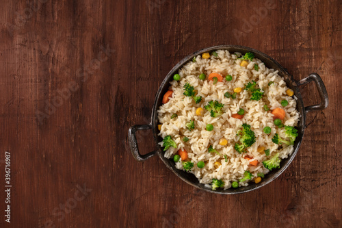 Stir-fried vegetable rice with broccoli, green peas and carrots, overhead shot on a dark rusitic wooden table with a place for text