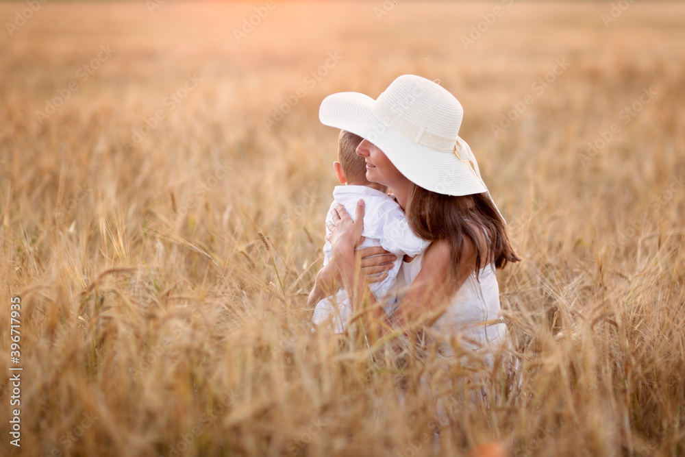Caucasian beautiful mother hugs her child son in the summer wheat field at sunset, summer and harvest, rest in the village