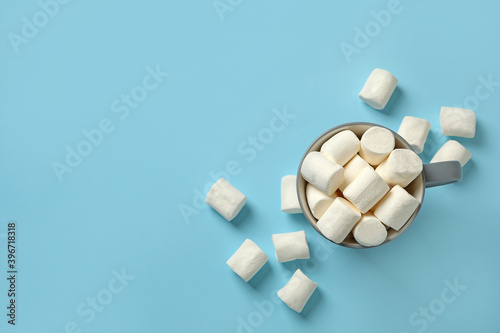 Cup with marshmallow on blue background, top view
