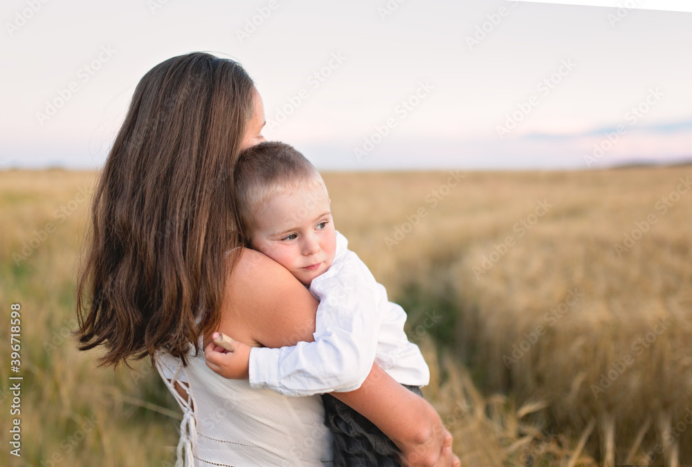 Caucasian beautiful mother hugs her child son in the summer wheat field at sunset, summer and harvest, natural products and relaxation in the countryside, motherhood Caucasian beautiful mother hugs her child son in the summer wheat field at sunset, summer and harvest, natural products and relaxation in the countryside, motherhood