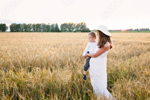 Caucasian beautiful mother hugs her child son in the summer wheat field at sunset, summer and harvest, natural products and relaxation in the countryside, motherhood