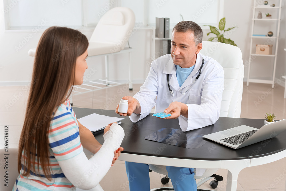 Fototapeta premium Young woman with broken arm visiting doctor in clinic