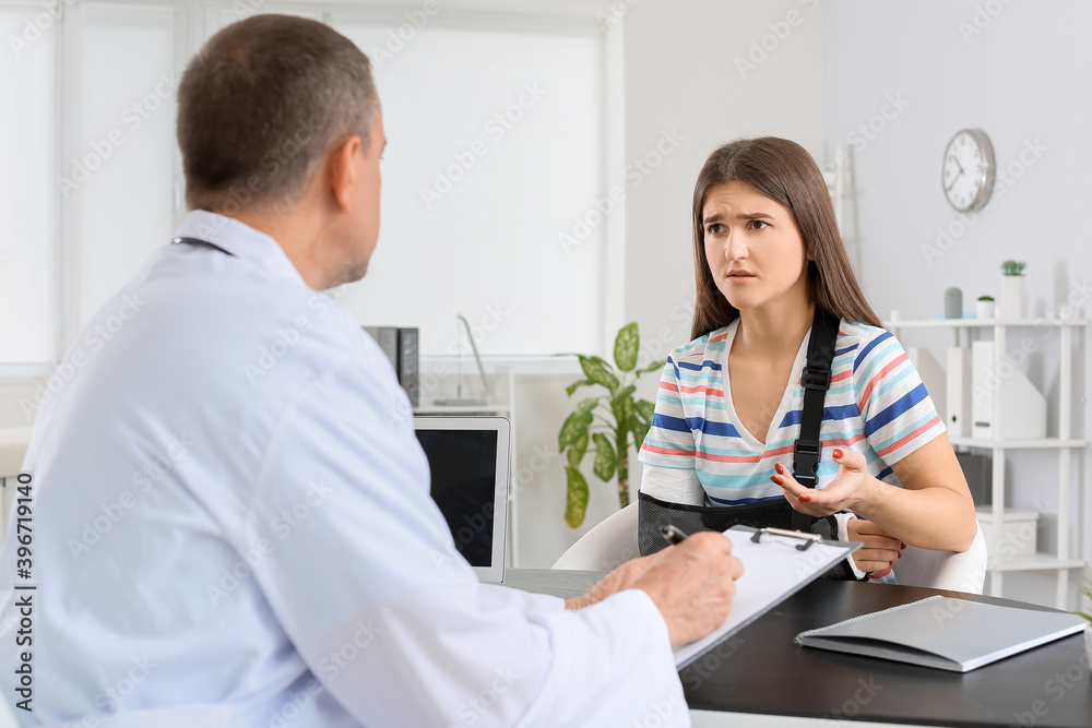 Fototapeta premium Young woman with broken arm visiting doctor in clinic