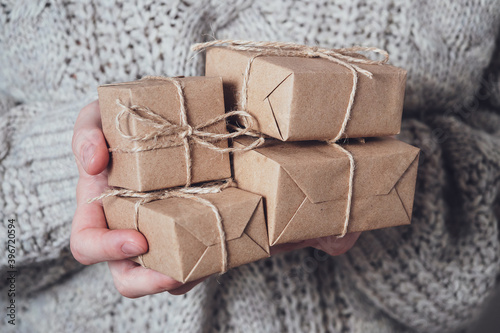 Gifts in women's hands, close-up. Monochrome, minimalist gift concept. A girl in a sweater holds gift boxes made of Kraft paper, tied with a string. Surprise background, greeting card