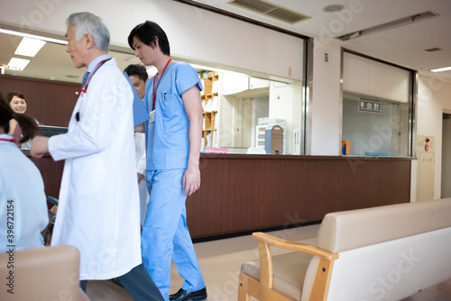 病院の廊下を会話しながら歩く大先輩の医師と若手医師 © Monet