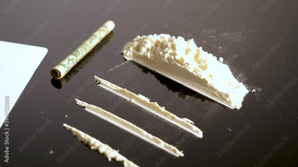 Lines of cocaine and a dollar bill. Cocaine lines shots on a black table glass. Cocaine powder, Credit card, close up, toned. Drug abuse concept. White poder on black table