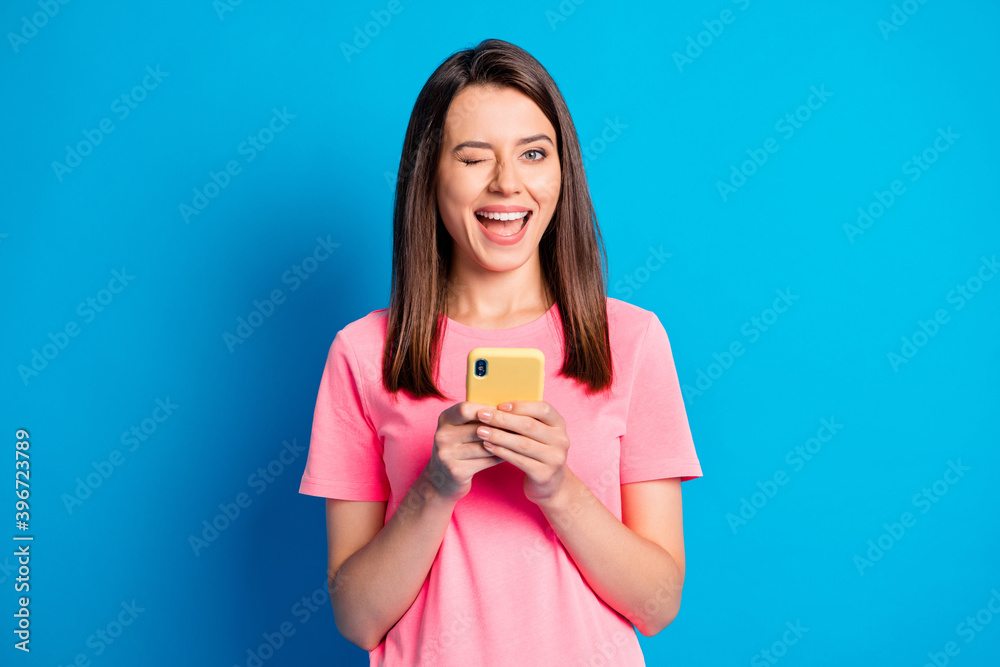 Photo portrait of happy positive brunette keeping mobile phone winking blinking isolated on bright blue color background Photo portrait of happy positive brunette keeping mobile phone winking blinking isolated on bright blue color background