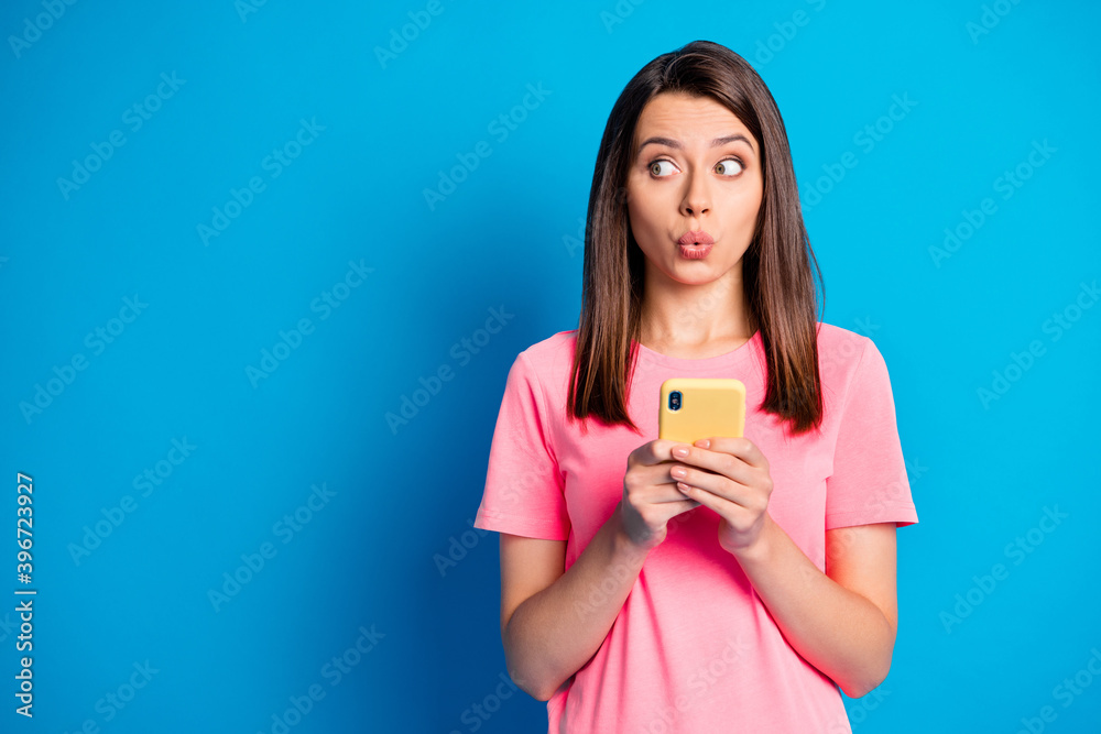 Photo portrait of curious young girl staring whistling looking copyspace holding smartphone isolated on bright blue color background Photo portrait of curious young girl staring whistling looking copyspace holding smartphone isolated on bright blue color background