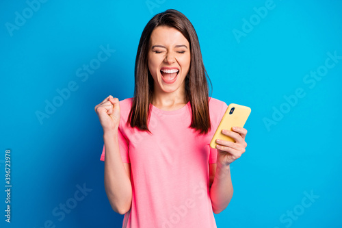 Photo portrait of cheerful young girl gesturing like winner closed eyes using smartphone isolated on bright blue color background