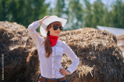 A woman in a cowboy hat and sunglasses in the hayloft.