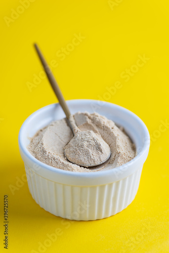 Sunflower lecithin in a bowl with a spoon on a yellow background.