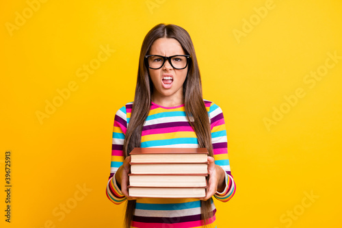 Photo portrait of irritated little girl keeping books grimacing don't want to do homework isolated on vibrant yellow color background