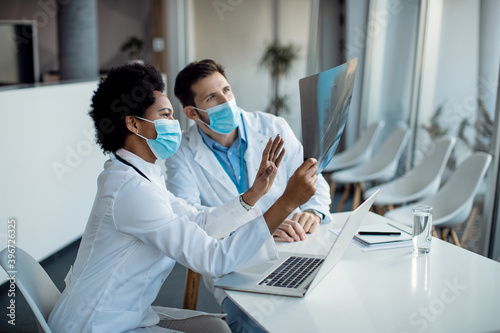 Two doctors cooperating while analyzing X-ray image and wearing face masks due to COVID-19 pandemic.