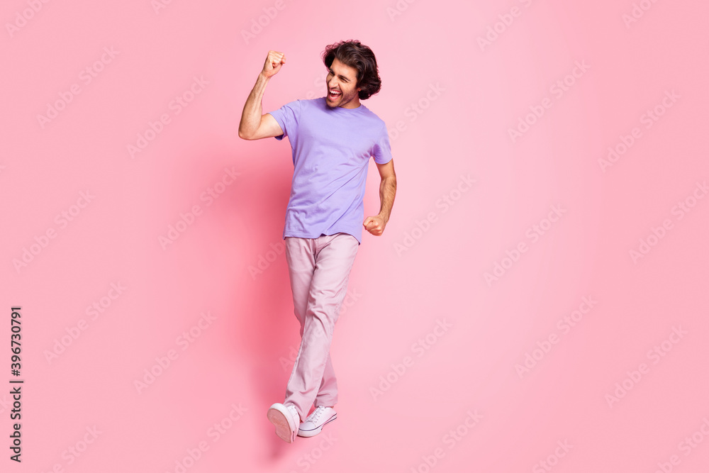 Full size photo of astonished fan person walking yell yes fist up wear purple isolated on pink color background Full size photo of astonished fan person walking yell yes fist up wear purple isolated on pink color background