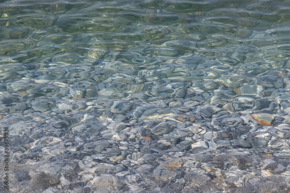 Transparent sea water with a pebble bottom, stone beach. Soft waves and ripple on clear water surface