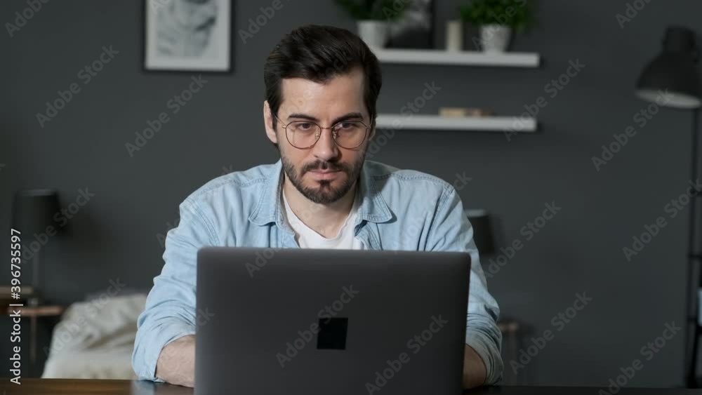 Young Man Freelancer Using Laptop, Typing, Scrolling, Surfing Web, Looking at the Screen. Professional Creative Millennial Sitting at His Desk in Home Office Young Man Freelancer Using Laptop, Typing, Scrolling, Surfing Web, Looking at the Screen. Professional Creative Millennial Sitting at His Desk in Home Office