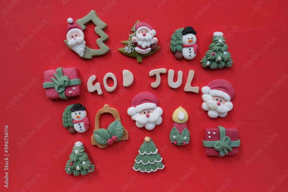 Creative swedish and norwegian Merry Christmas, God Jul, with wooden letters and marzipan Christmas symbols over red color background