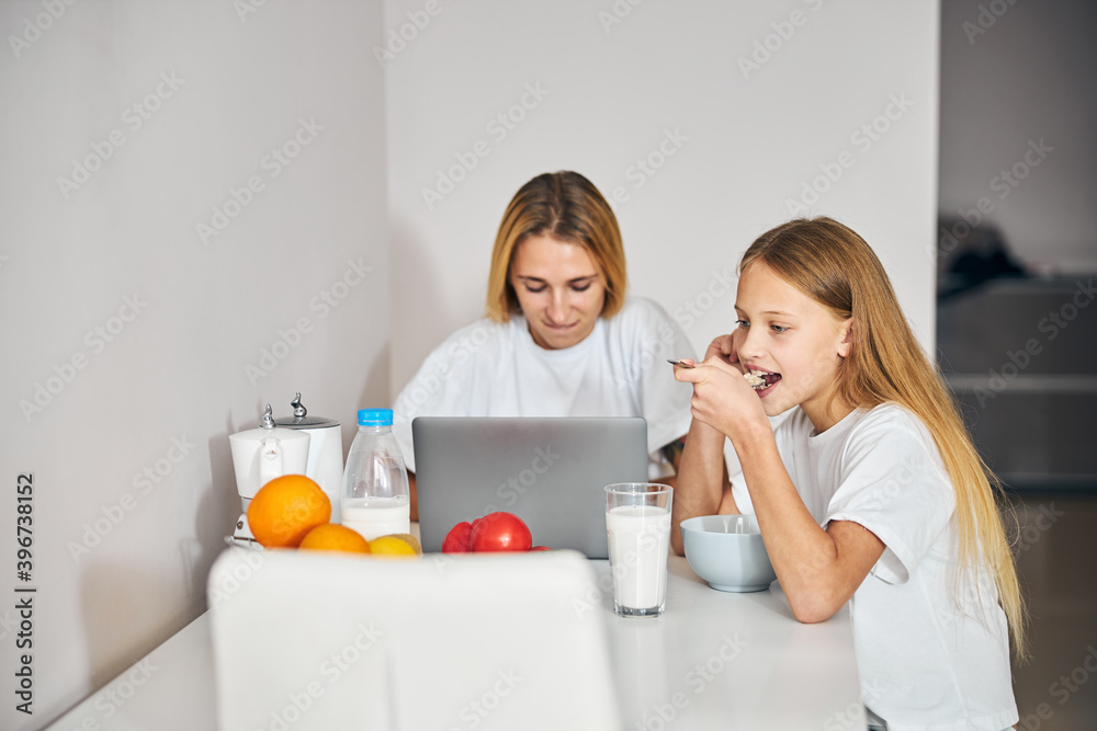 Thoughtful daughter and busy mother sitting at the kitchen table Thoughtful daughter and busy mother sitting at the kitchen table