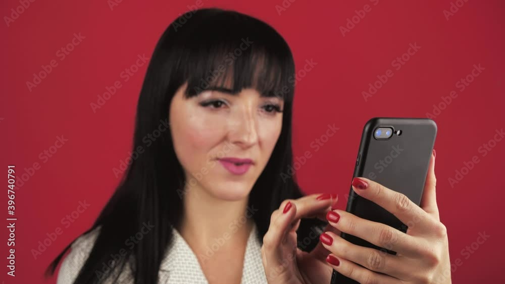 happy woman excitingly flips through the news feed in a mobile phone over red background. happy woman excitingly flips through the news feed in a mobile phone over red background.