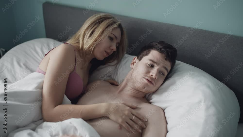 Sweet couple lying in white bed under covers and touching each other. Pretty girl caring guy in bedroom on honeymoon. Newlyweds huging naked or nude in apartment or hotel. Love, relationship concept. Sweet couple lying in white bed under covers and touching each other. Pretty girl caring guy in bedroom on honeymoon. Newlyweds huging naked or nude in apartment or hotel. Love, relationship concept.