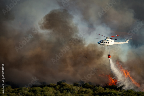 Smoke and huge fire and blurred helicopter with bambi bucket dumping water