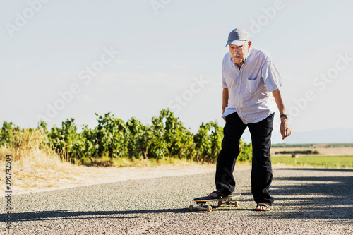 Ottantenne si diverte con ad andare in skateboard in una strada di campagna   photo