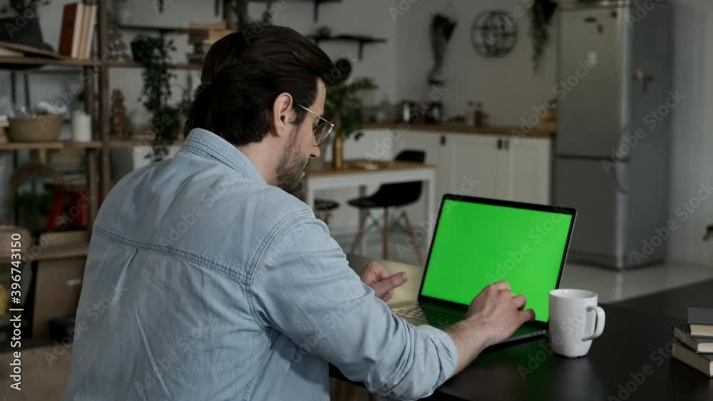 Over the shoulder shot of man working online on laptop with green screen display in living space Over the shoulder shot of man working online on laptop with green screen display in living space
