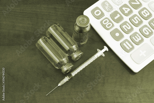 Calculator, vaccine and syringe on wooden background. Cost of vaccine and vaccination concept. photo