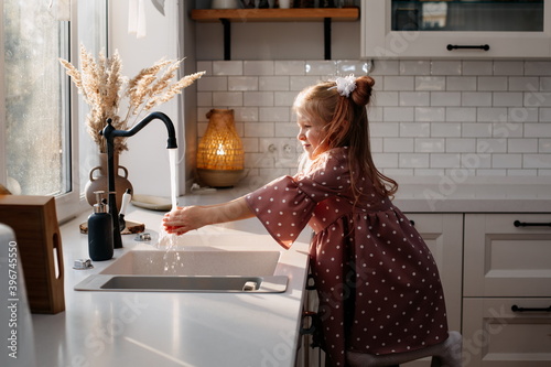 little 5 year old girl washes her hands at home in the kitchen